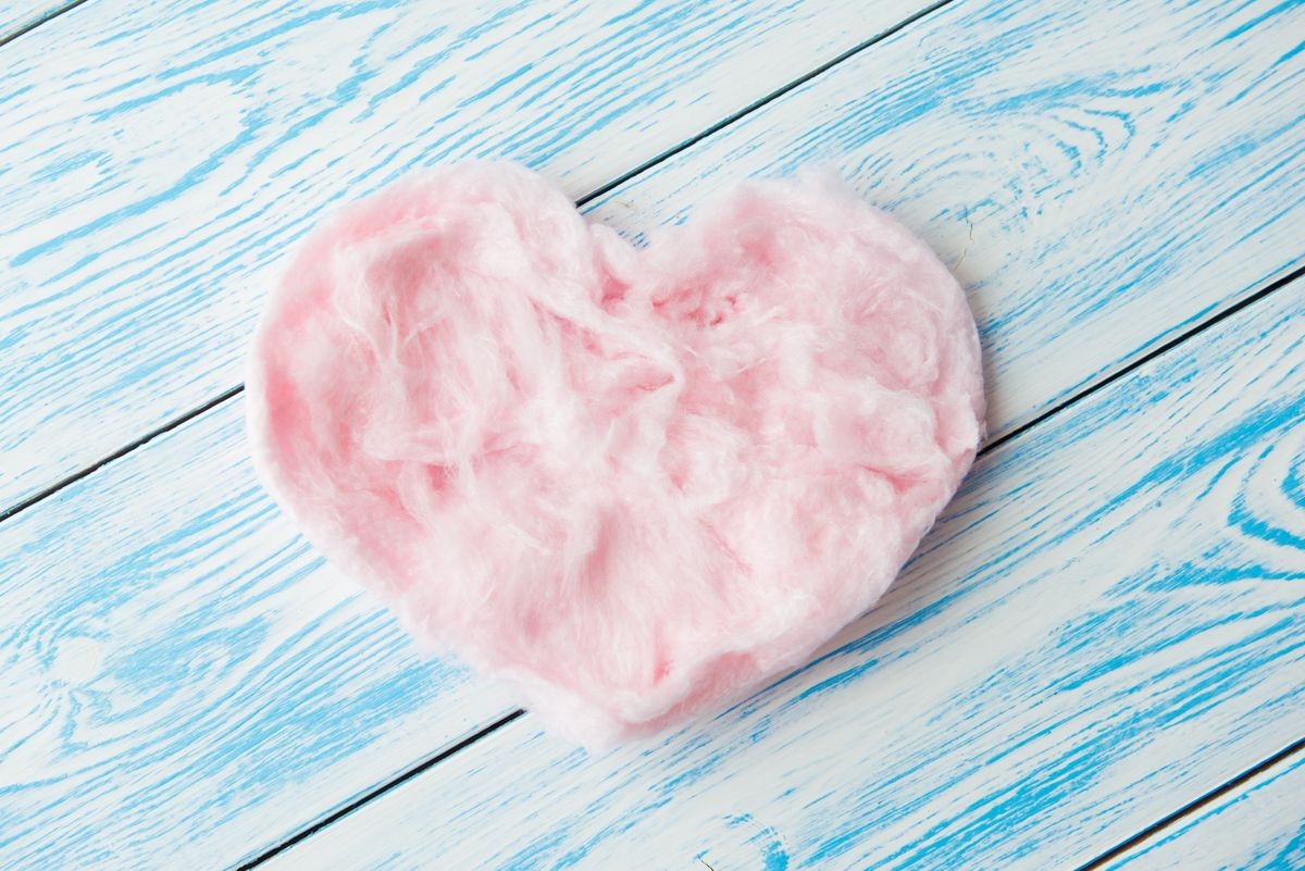 Sweet cotton candy in heart shape on blue wooden background